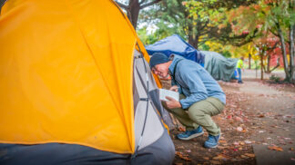 man crouched down speaking to someone in a tent
