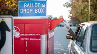 person in a car dropping their election ballot in a drop box