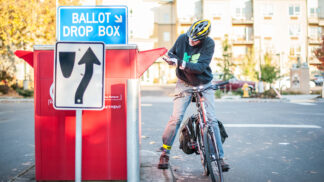 cyclist dropping their election ballot in a drop box