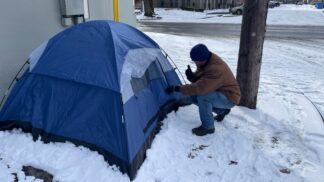 man crouched down in front of a tent in the snow